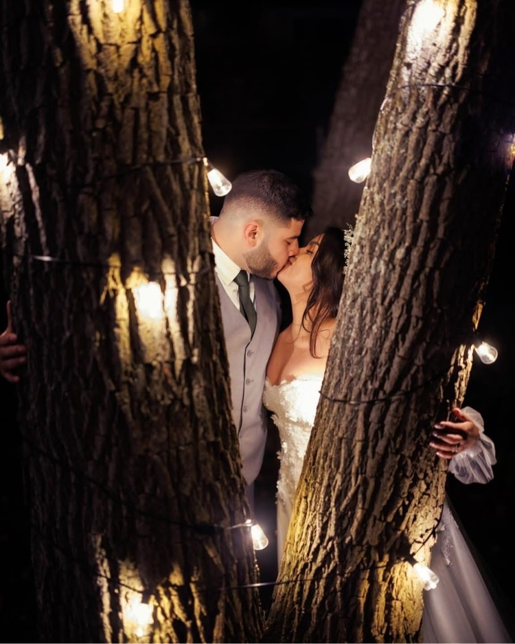 Wedding — couple kissing between trees with string lights at night