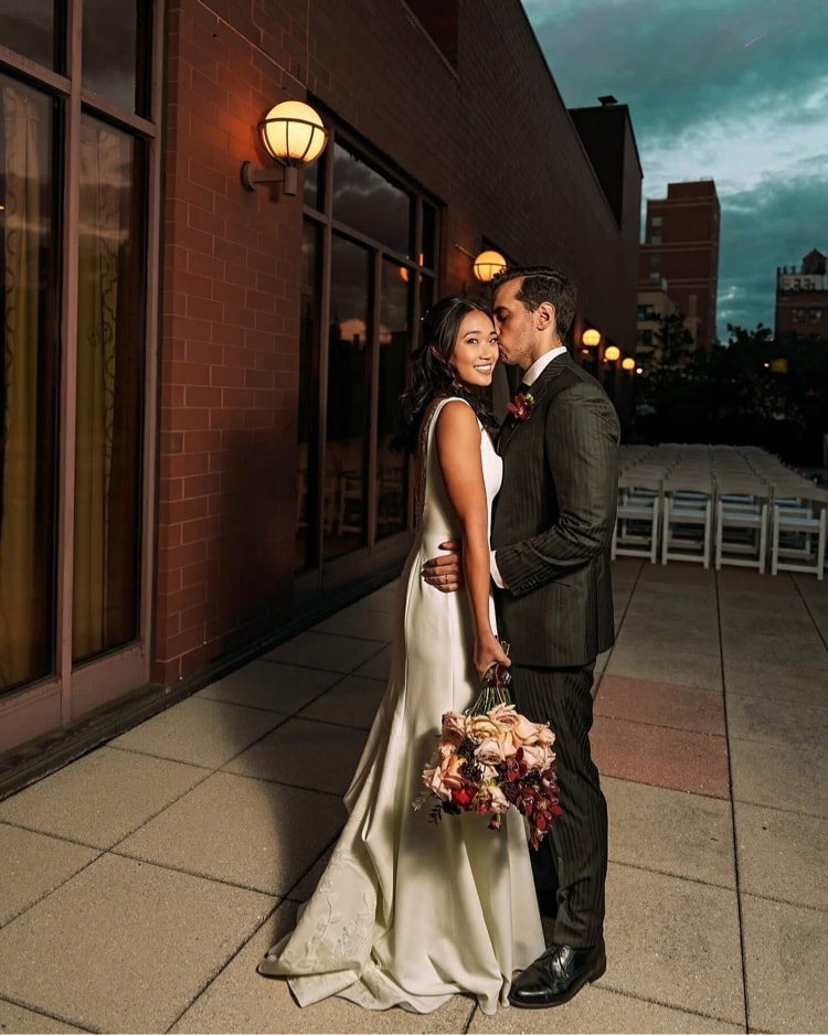 Bride and groom on rooftop at dusk, groom kissing bride on the cheek