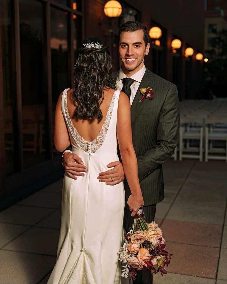 Groom smiling with bride from behind on rooftop at night
