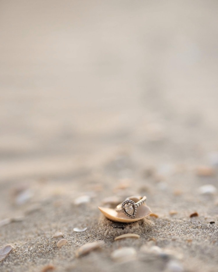 Engagement ring resting in a seashell on the beach