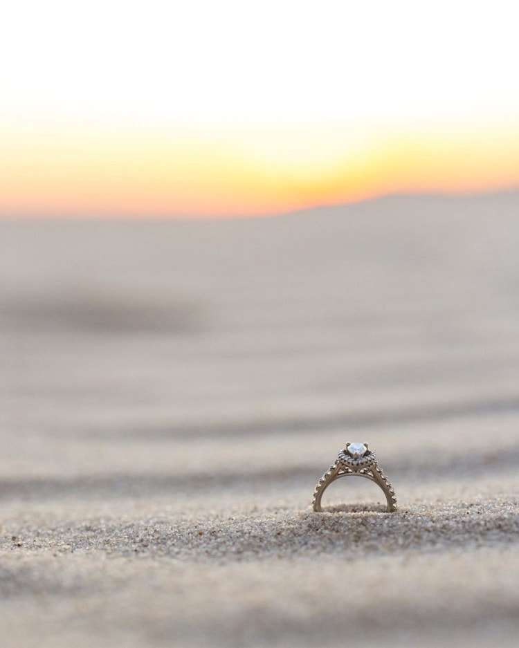 Engagement ring standing in sand at sunset